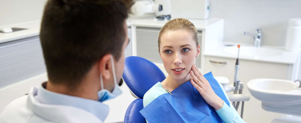 A young woman looks at the dentist and touches her cheek.