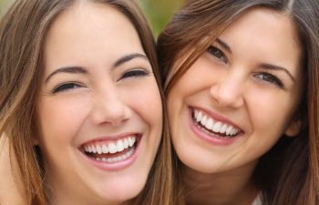 Two young women laugh while presenting beautiful smiles.