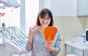 A happy mature woman in a dental office looking at her perfect teeth in a mirror.